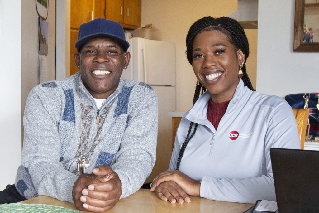 Female care provider sitting and smiling at kitchen table with middle-aged male member