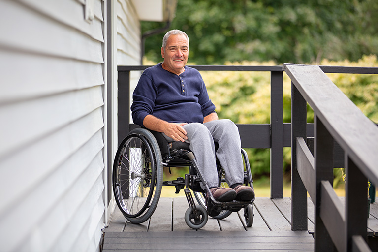 One Care member in wheelchair and blue shirt smiling outdoors on his home porch