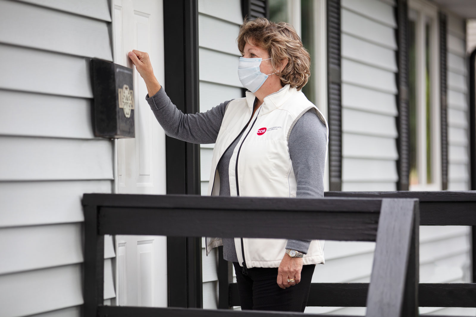 Female care provider with mask wearing CCA vest knocking on a member's front door