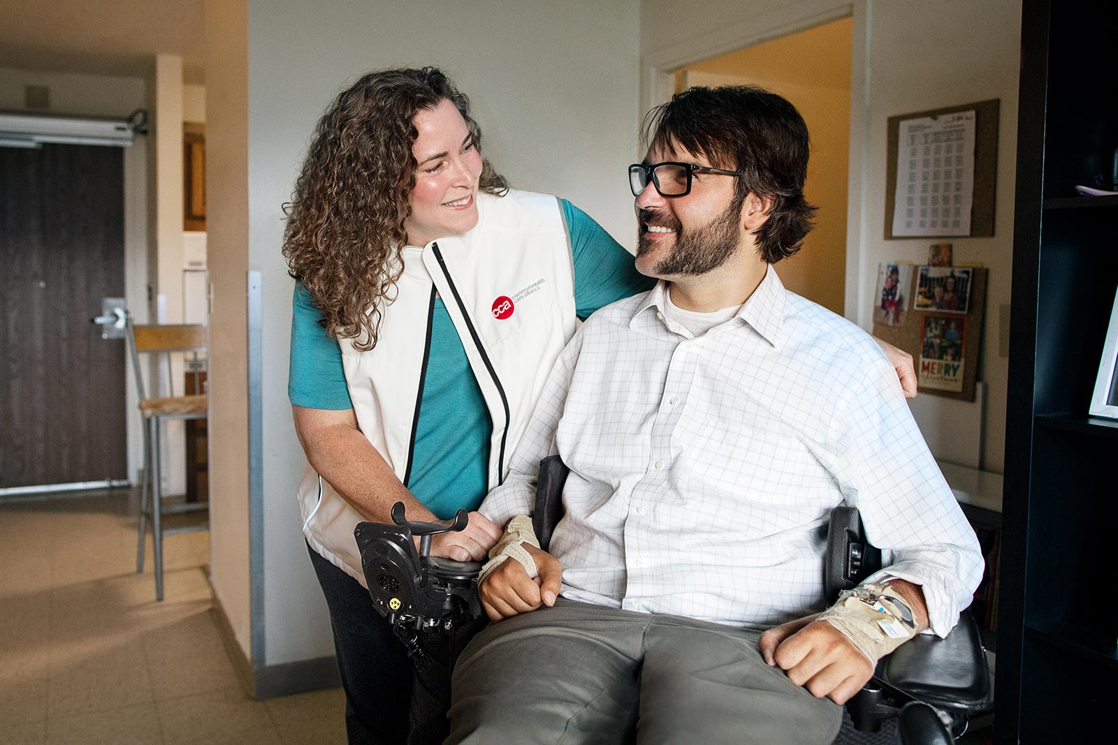 Disabled man in wheelchair smiling in his home with female care partner