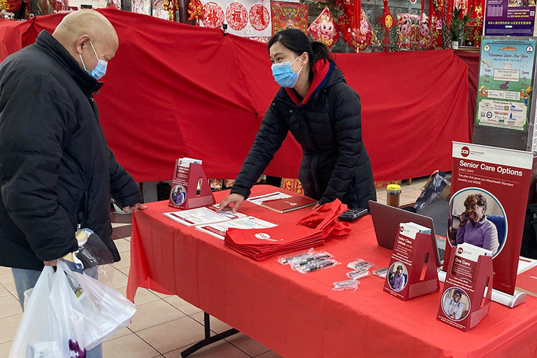 CCA employee at table with promotional items speaks to man inside market