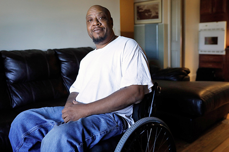CCA member seated in wheelchair in his living room