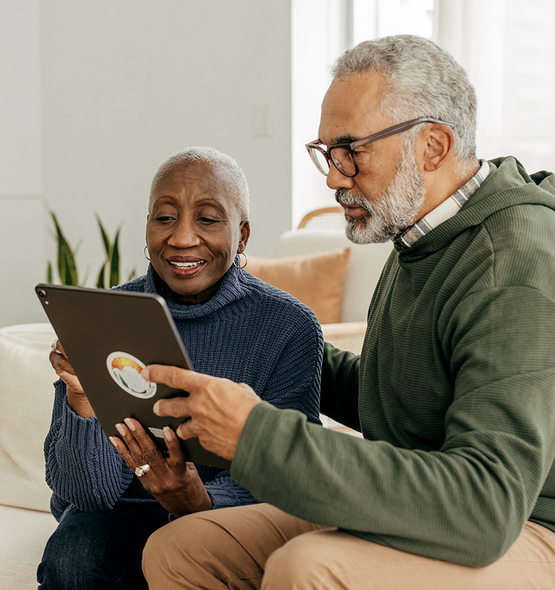 Older male patient seated with mask on listening to female nurse with mask with her hand on his shoulder at doctor's office