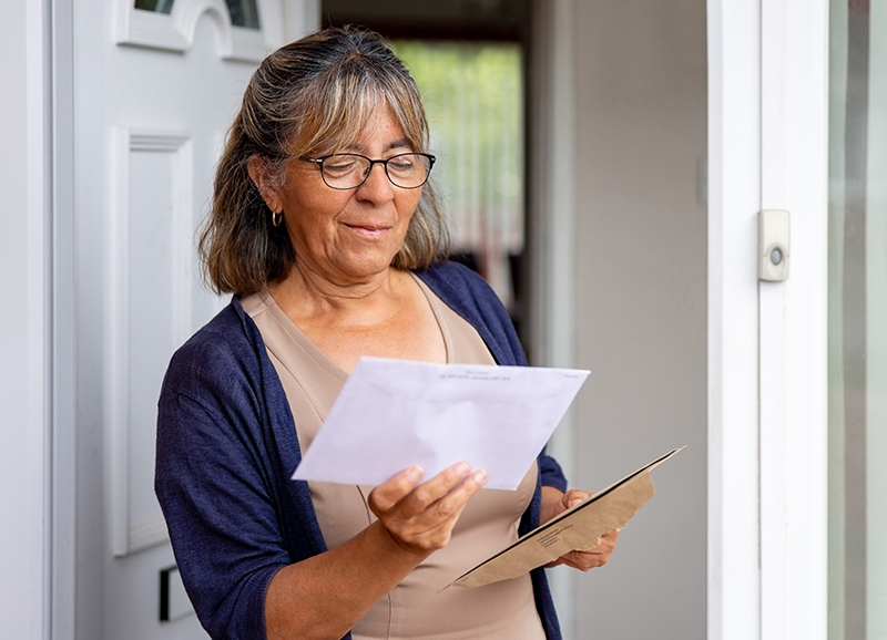 woman with shoulder length hair looking at mail on the doorstep with the door open.
