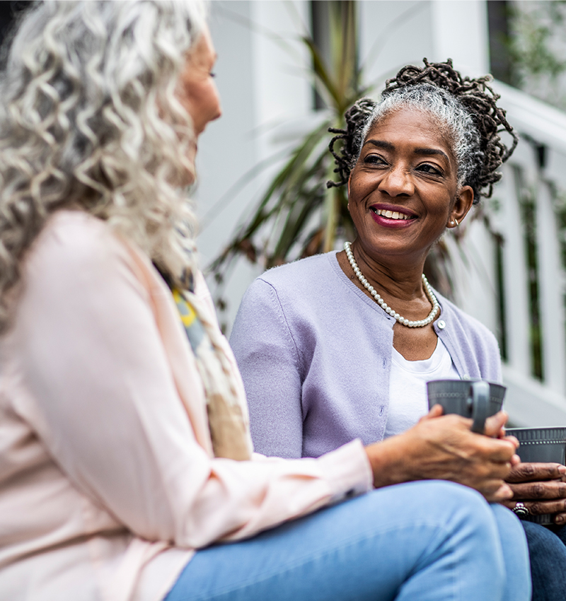 african american woman smiling and talking to another woman on steps drinking a beverage in a mug.