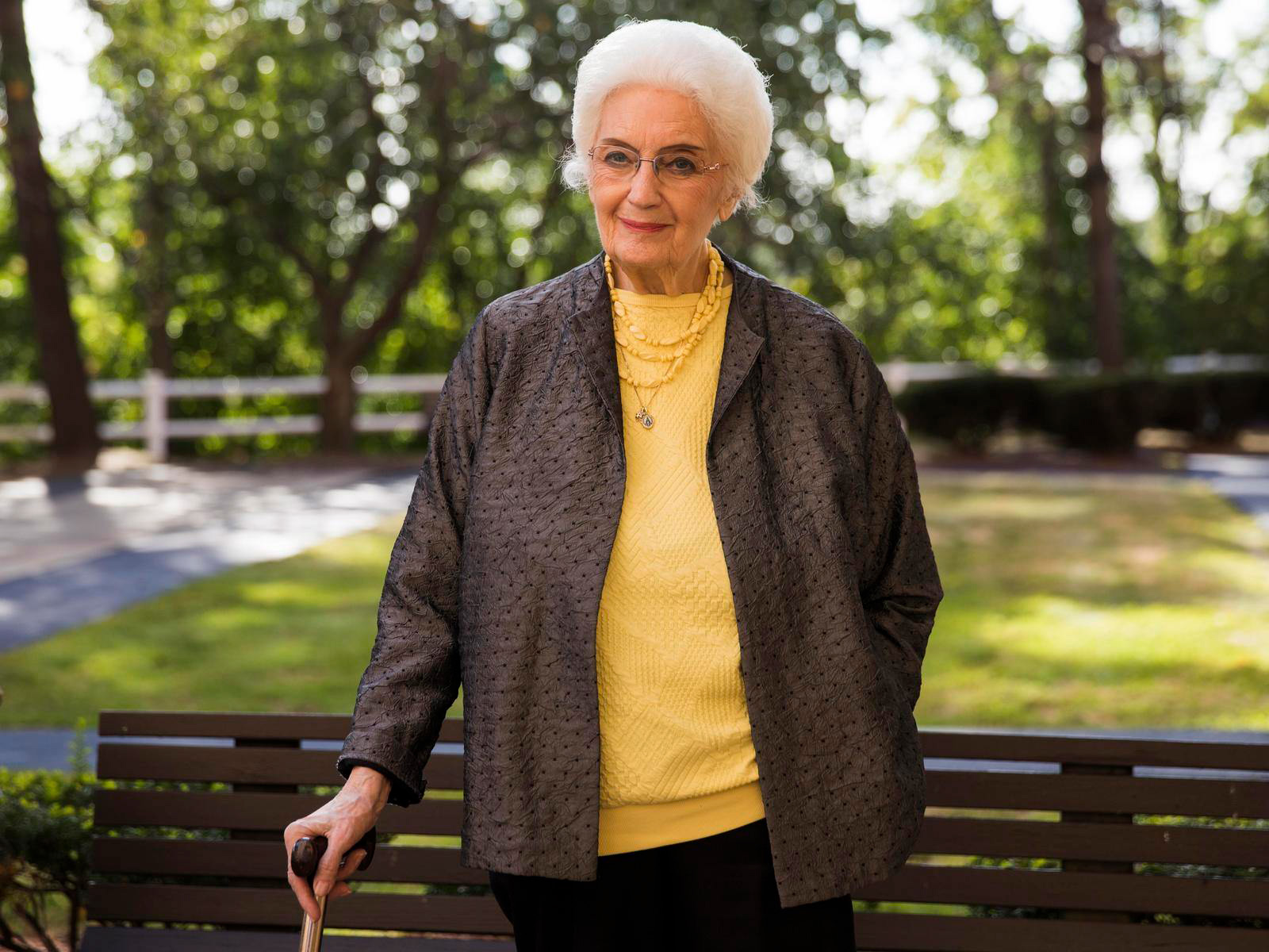 Senior woman enjoying the outdoors standing in front of park bench holding her cane
