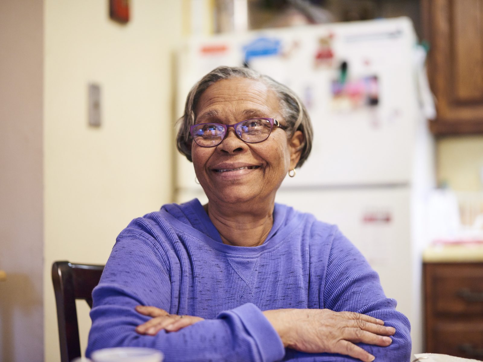 Senior woman seated at table in her kitchen, smiling at camera