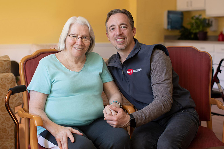 Elderly woman and male care partner sitting in her home smiling and holding hands