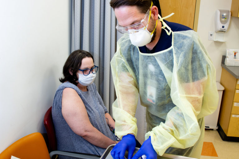 Patient seated in CCA Primary Care office with doctor reaching for syringe