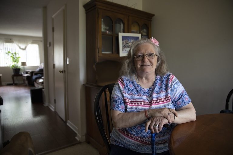 Woman with glasses and white hair sits at a table in her home