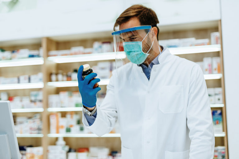 A male pharmacist wearing protective gear inside pharmacy