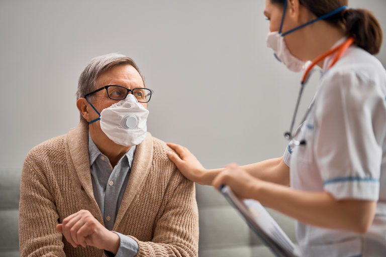 A female medical worker wearing a surgical mask talking to an older man wearing a surgical mask