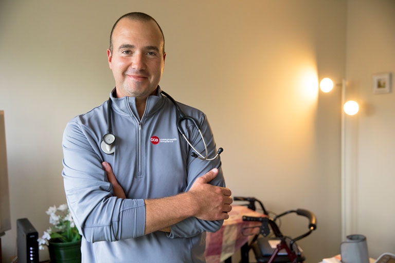 Male care partner standing and smiling with arms crossed in CCA jacket with stethoscope around neck