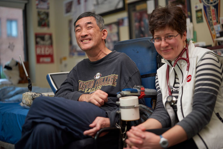 Older Asian man in wheelchair smiling in his home with female care partner