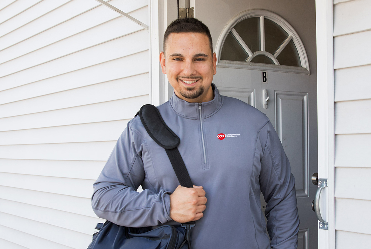 Young male professional standing in front of his home with professional bag over shoulder wearing CCA jacket