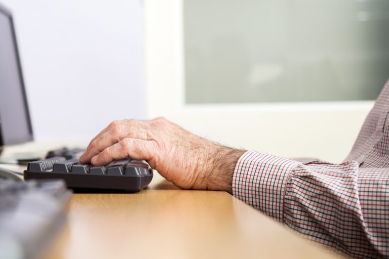 An older man typing on a desktop computer keyboard