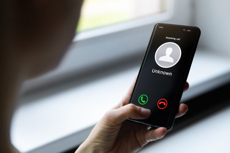 COVID-19 Vaccine Scam Alert: Five Steps to Protect Yourself Person holding a smartphone with an incoming unknown call displayed on the screen