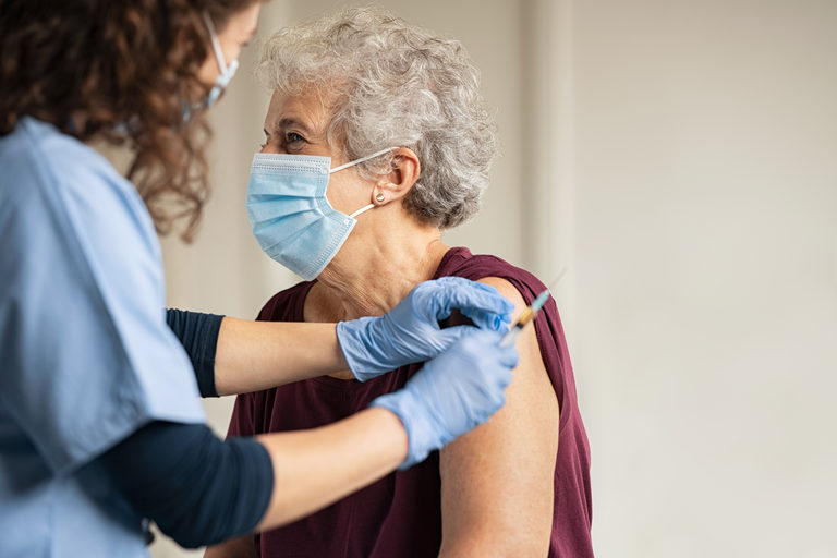 COVID-19 Vaccine Basics and What to Expect After You’re Vaccinated A nurse giving a shot in the upper arm of an older woman wearing a surgical mask