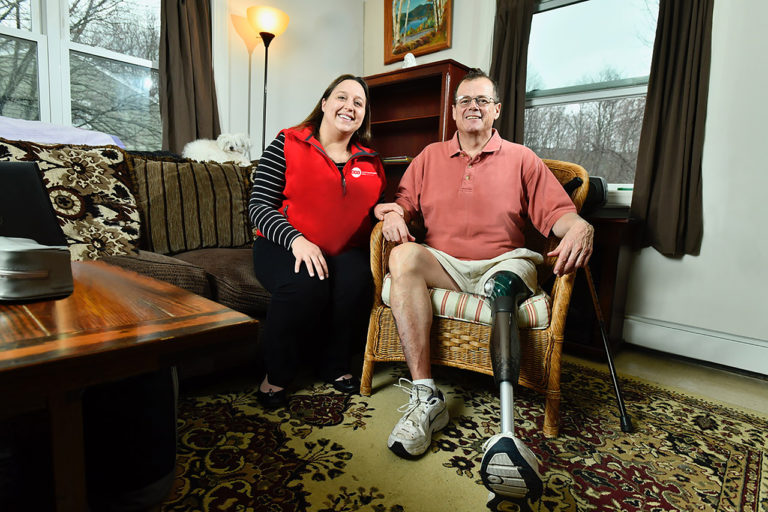 Retired Marine and CCA member Mike sitting and smiling at home with his care partner showing his prosthetic leg