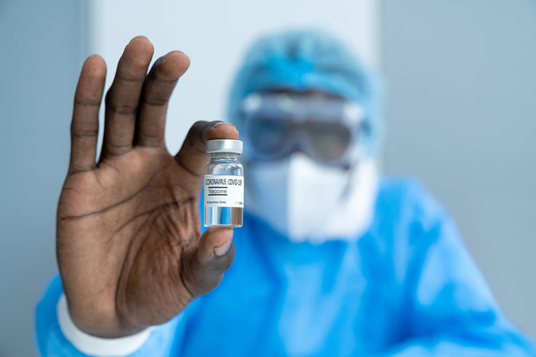 Medical worker wearing personal protective equipment holding a COVID-19 vaccine vial
