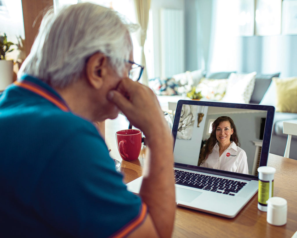 Elderly man participating in a virtual medical visit at home on his laptop