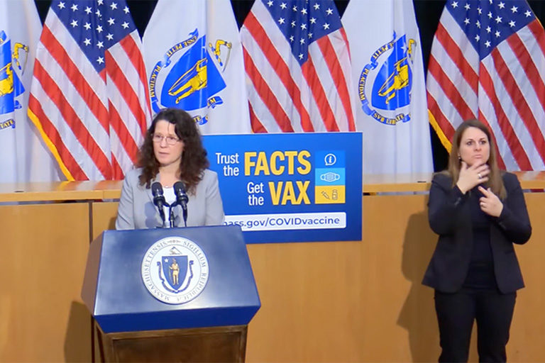 CCA's Kelli Barrieau speaking at podium with Massachusetts and US flags in background