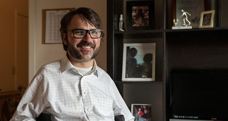 Disabled man in wheelchair smiling in his home study