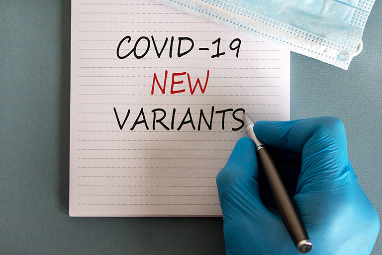 Hand wearing blue medical glove writing "COVID-19 New Variants" on a notepad