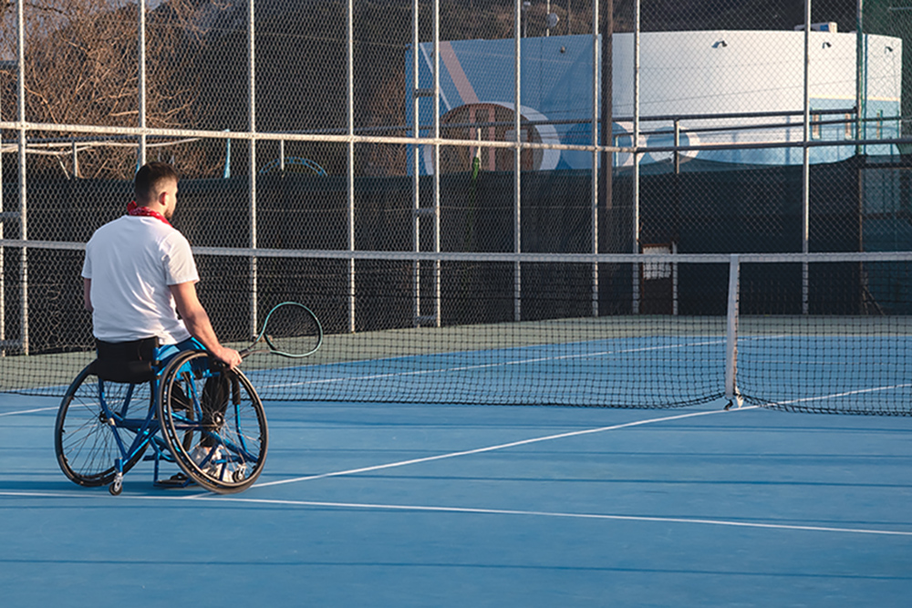 Back view at young man in wheelchair at tennis court.