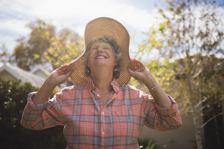 Close up of smiling senior woman wearing sun hat in backyard on sunny day