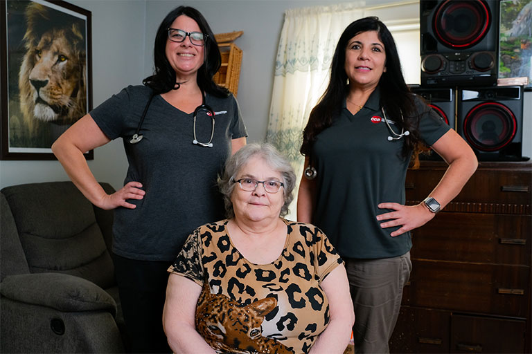 CCA member Cynthia sitting in her living room with two members of the CCA Care team standing behind her. 