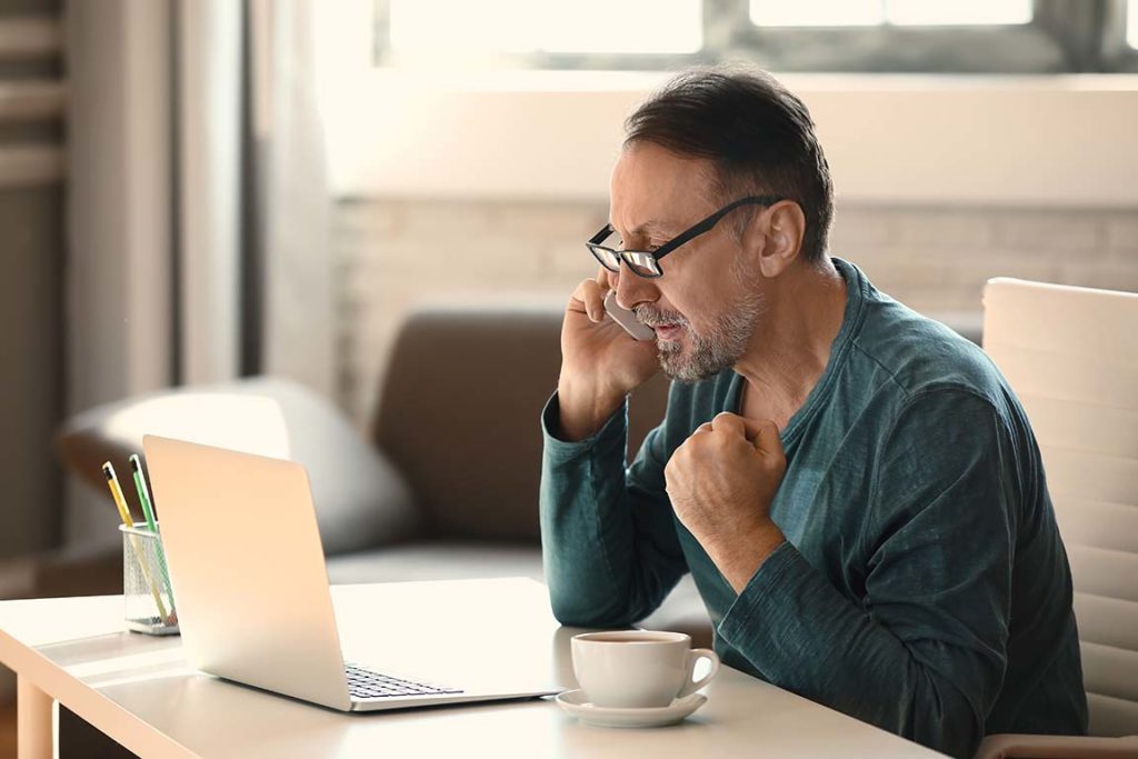 Senior man calling while looking at information on his laptop