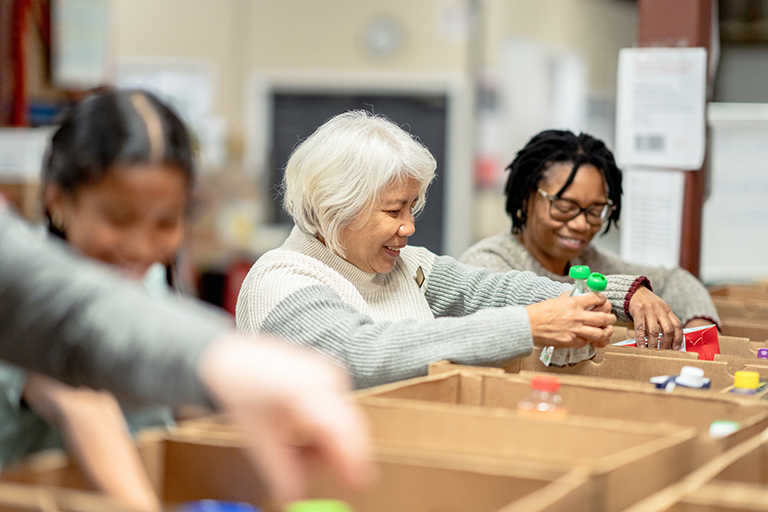 People putting food in boxes while volunteering at a food bank