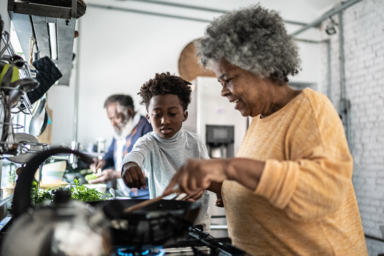 An image of an older woman cooking a meal with her grandson.