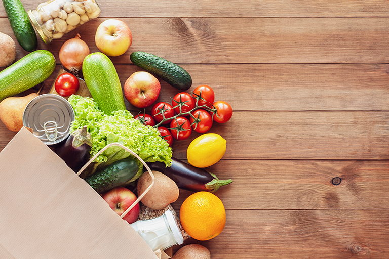 A bag of healthy groceries, including fruits, vegetables, nuts, and milk. 