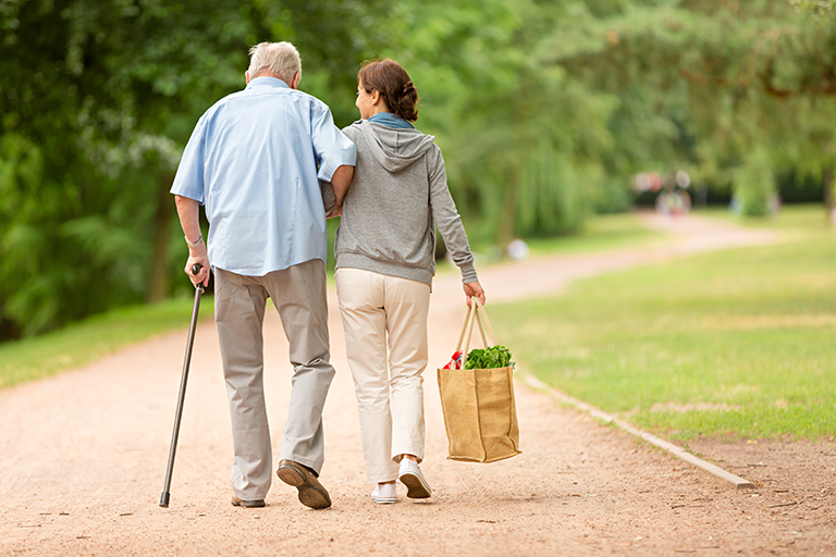 An image of a community health worker carrying food for an older adult and helping him walk.