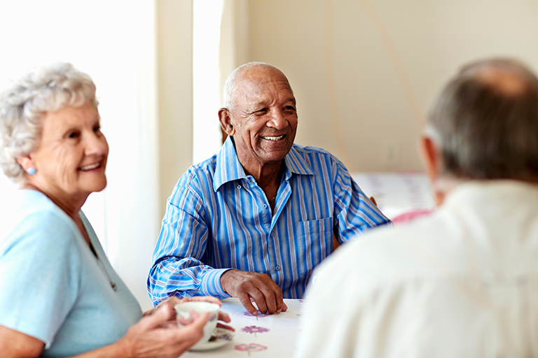 Three older adults sitting around a table at a nursing home socializing and drinking coffee.