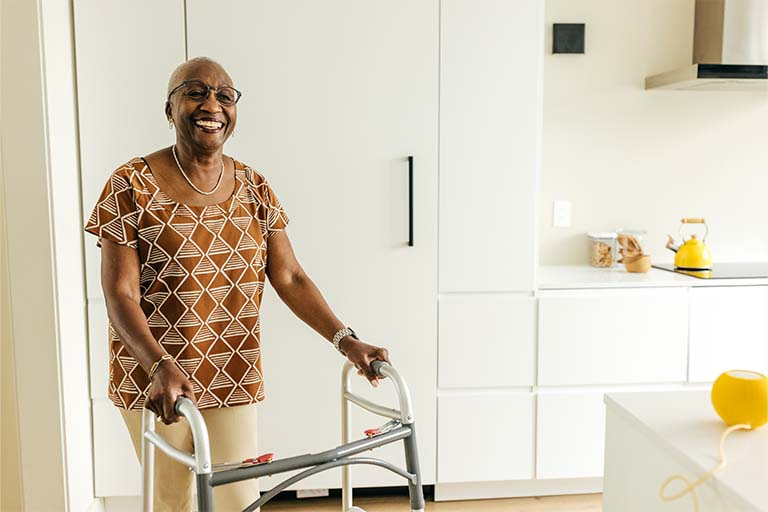 Coming September 2024: New Platform for Ordering Durable Medical Equipment, Prosthetics, Orthotics, and Medical Supplies Older woman in her home smiling at the camera while holding a walker